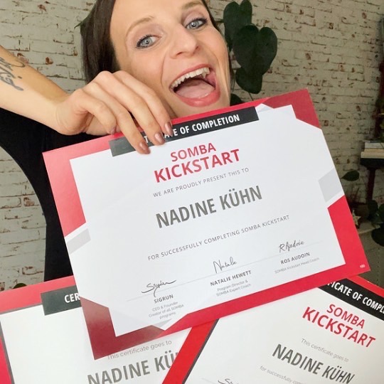 Brunette woman with a huge smile on her face, showing her 3 certificates of completing Somba Kickstart 
