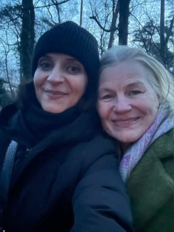 Two women outdoors, one wear a black coat, the other one a green one. Posing for a selfie