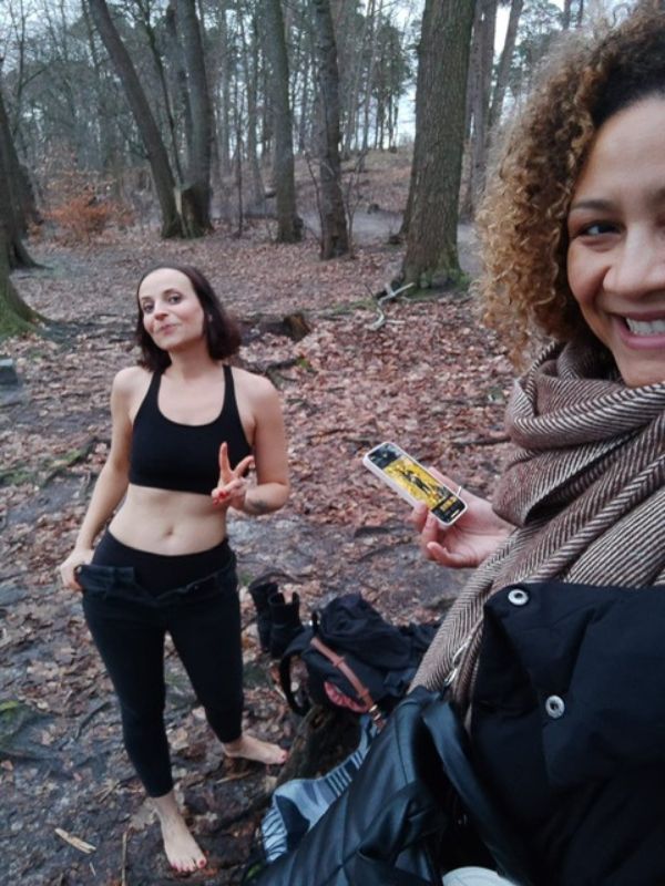 Two women outdoors, smiling at the camera. The woman in the back is getting ready for her swim in cold water.