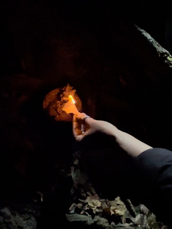 Dark background with a little fire. A hand holding a piece of paper into the fire.
