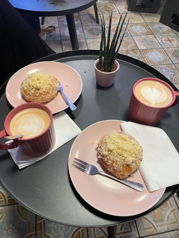 In a café: two vegan donuts on pink plates, and two cups of latte macchiato.