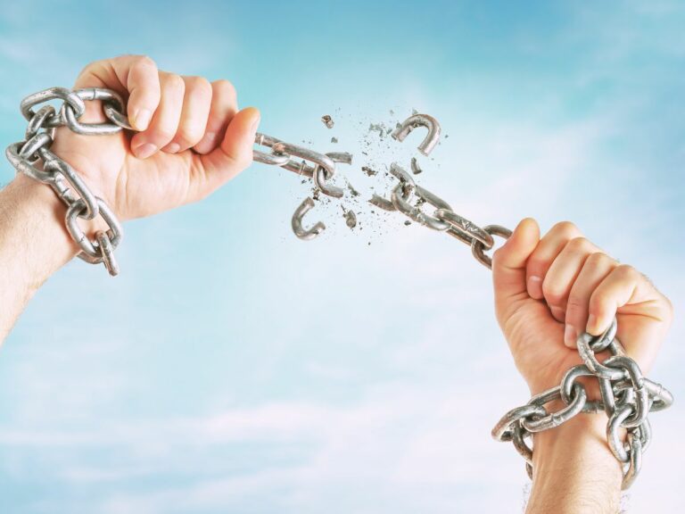 Two hands breaking a metal chain. In the background blue sky.