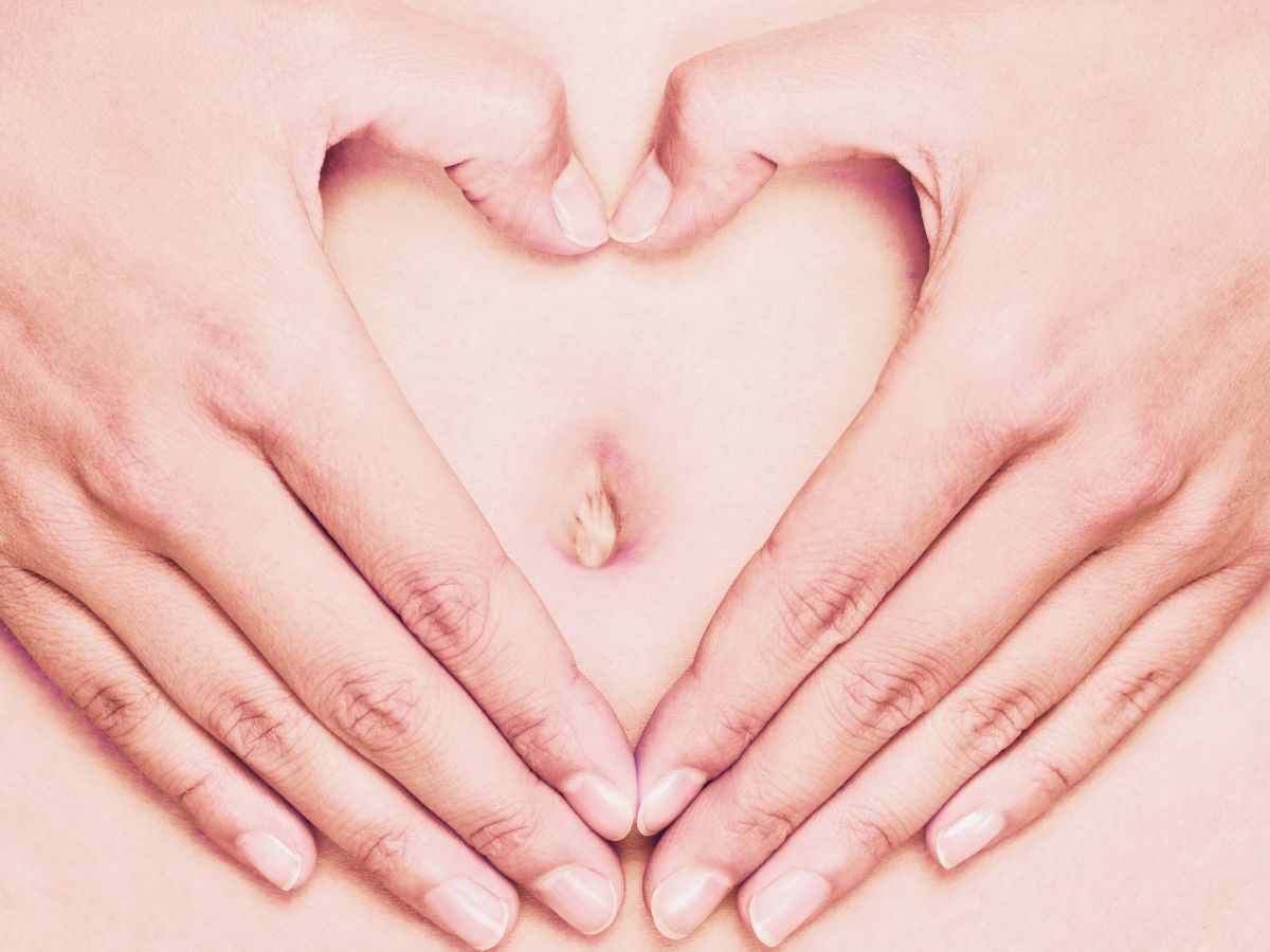 two hands forming a heart over a woman's belly button.