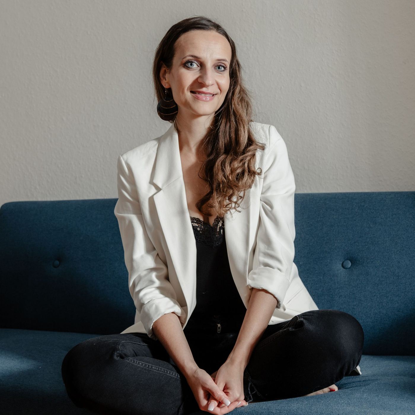 Nadine Kühn sitting on a blue sofa in a white blazer, smiling at the camera