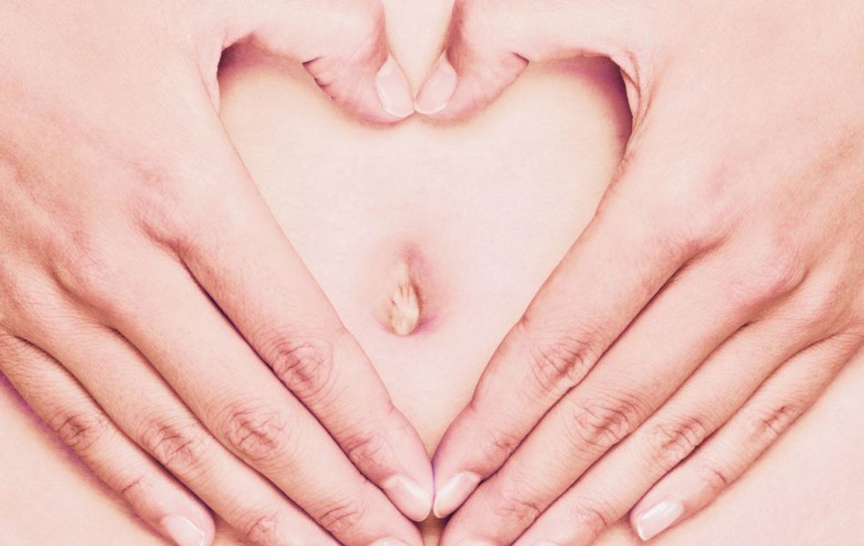 two hands forming a heart over a woman's belly button.